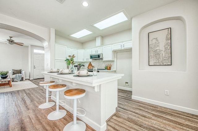 kitchen featuring arched walkways, light countertops, stainless steel microwave, light wood-type flooring, and a kitchen breakfast bar