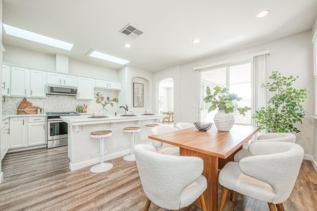 dining space with arched walkways, recessed lighting, visible vents, baseboards, and light wood-type flooring