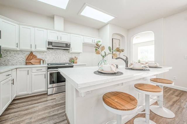 kitchen with white cabinets, light wood finished floors, stainless steel appliances, and backsplash