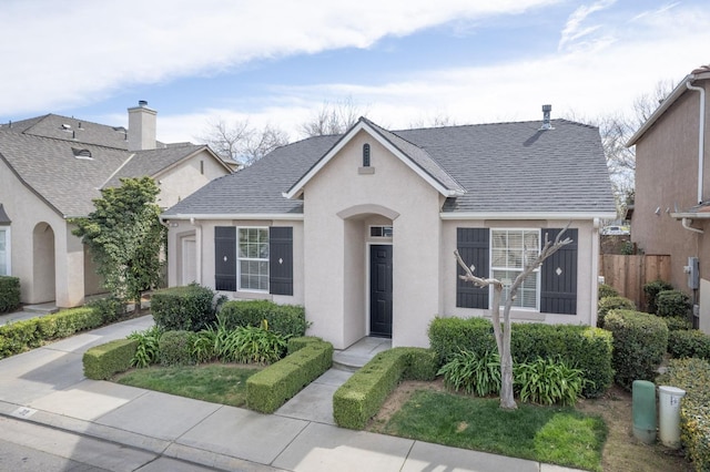 view of front of home featuring roof with shingles, fence, and stucco siding