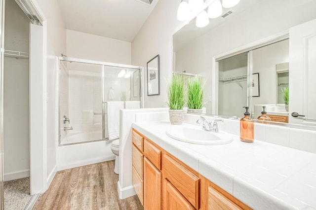 bathroom with visible vents, bath / shower combo with glass door, toilet, wood finished floors, and vanity