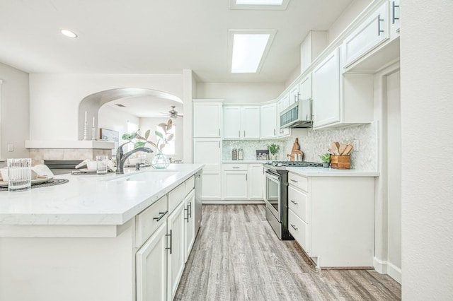 kitchen featuring tasteful backsplash, appliances with stainless steel finishes, light wood-type flooring, white cabinetry, and a sink