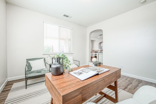 home office featuring arched walkways, wood finished floors, visible vents, and baseboards