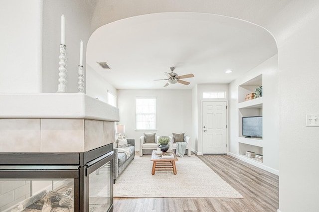 living area with baseboards, visible vents, ceiling fan, wood finished floors, and built in shelves