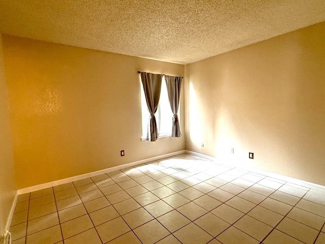 empty room with light tile patterned floors, baseboards, and a textured ceiling