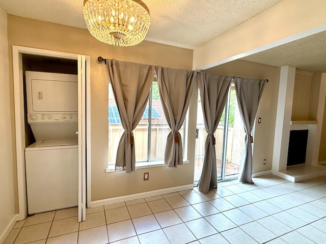 unfurnished room featuring a textured ceiling, a chandelier, stacked washer / drying machine, and light tile patterned flooring