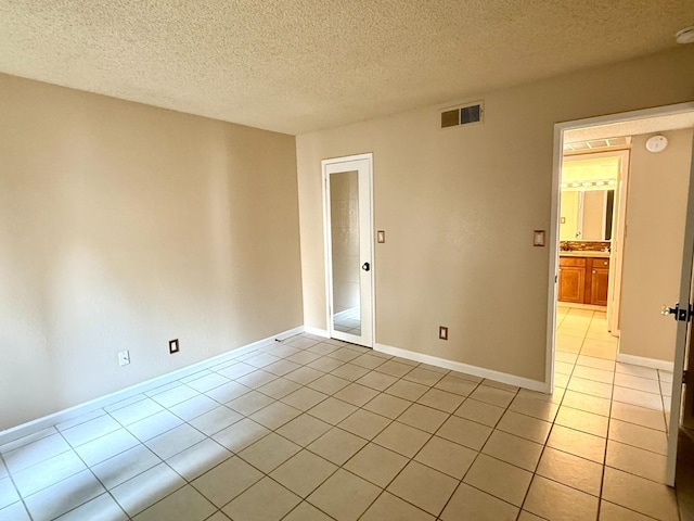 spare room with a textured ceiling, light tile patterned flooring, visible vents, and baseboards