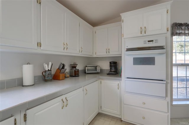 kitchen featuring oven, white cabinetry, vaulted ceiling, light countertops, and a warming drawer