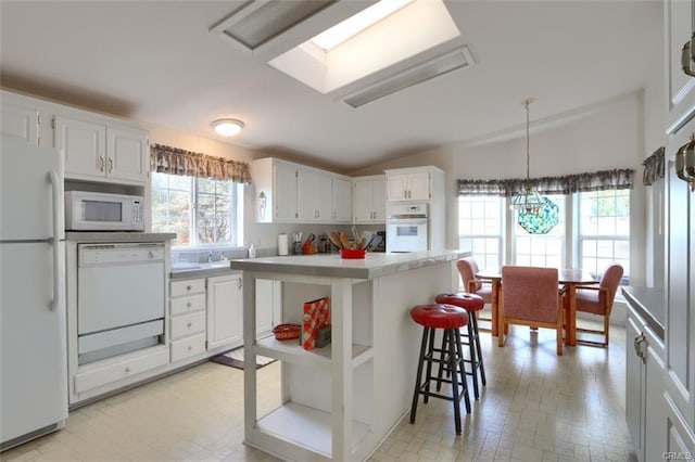 kitchen with white appliances, lofted ceiling, a breakfast bar area, light countertops, and white cabinetry