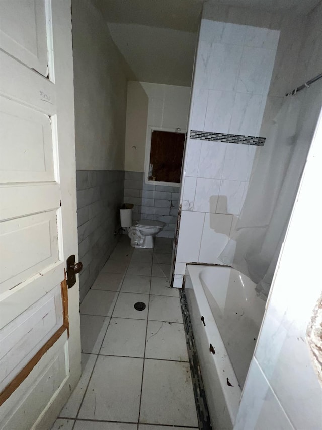 bathroom featuring a tub to relax in, tile walls, toilet, and tile patterned floors