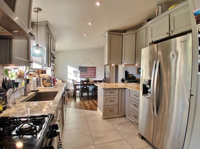 kitchen with range with gas stovetop, stainless steel fridge with ice dispenser, light stone counters, a peninsula, and light tile patterned flooring