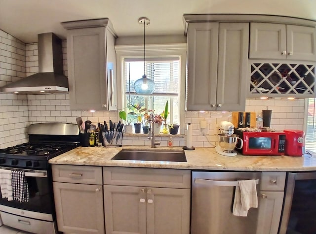 kitchen with light stone counters, decorative backsplash, appliances with stainless steel finishes, a sink, and wall chimney range hood