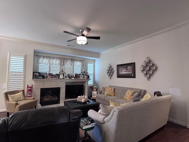 living room with visible vents, a tiled fireplace, ceiling fan, ornamental molding, and dark wood-style flooring