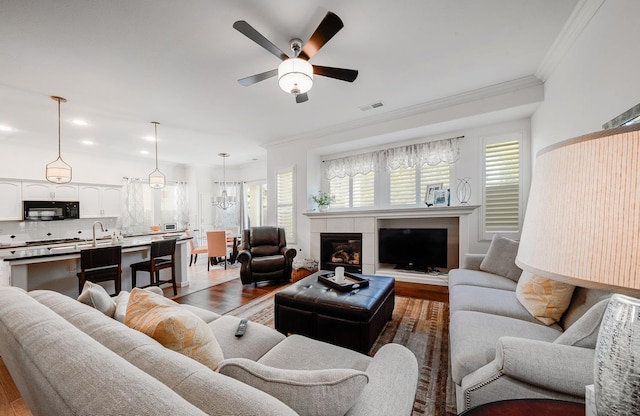 living room featuring ceiling fan, a fireplace, dark wood finished floors, ornamental molding, and visible vents