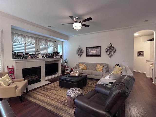 living area featuring arched walkways, dark wood-style flooring, crown molding, visible vents, and a fireplace with flush hearth