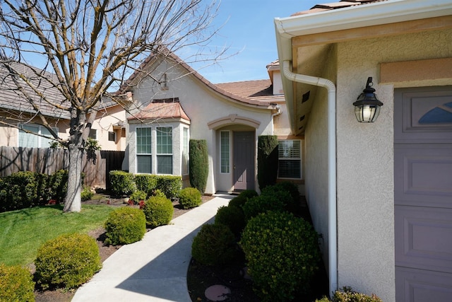 property entrance with stucco siding, fence, and a lawn