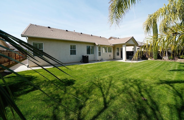 rear view of house with a tiled roof, a lawn, a fenced backyard, a patio, and stucco siding
