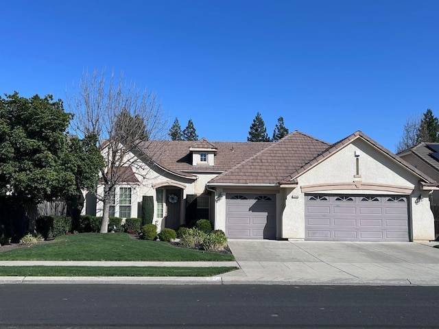 view of front of property with a garage, driveway, a tile roof, a front yard, and stucco siding