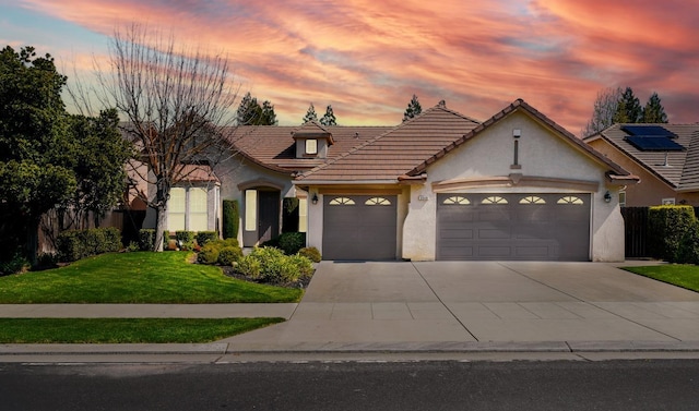 view of front of property with a yard, an attached garage, a tile roof, concrete driveway, and stucco siding
