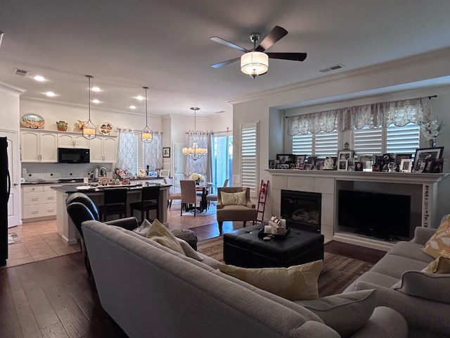 living area featuring ornamental molding, visible vents, dark wood finished floors, and ceiling fan with notable chandelier