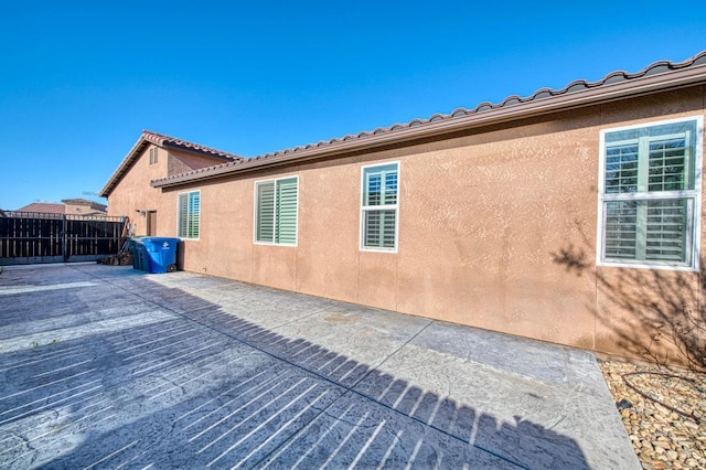 rear view of house featuring a tiled roof, fence, a patio, and stucco siding