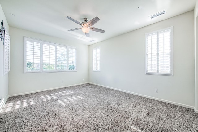 carpeted spare room with a ceiling fan, a wealth of natural light, visible vents, and baseboards