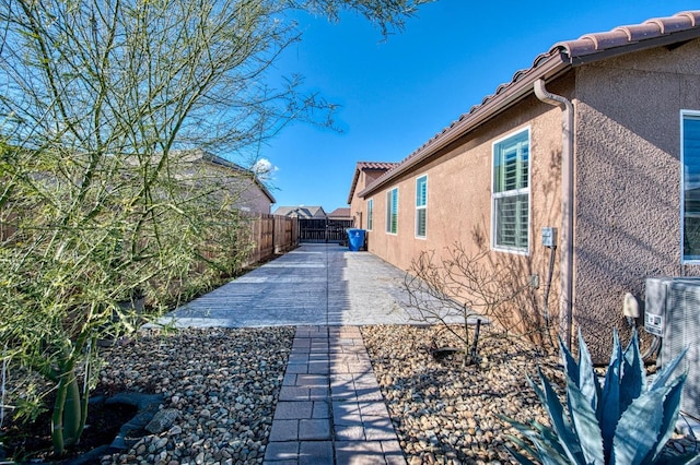 view of side of home featuring central AC unit, a patio, a tile roof, fence, and stucco siding