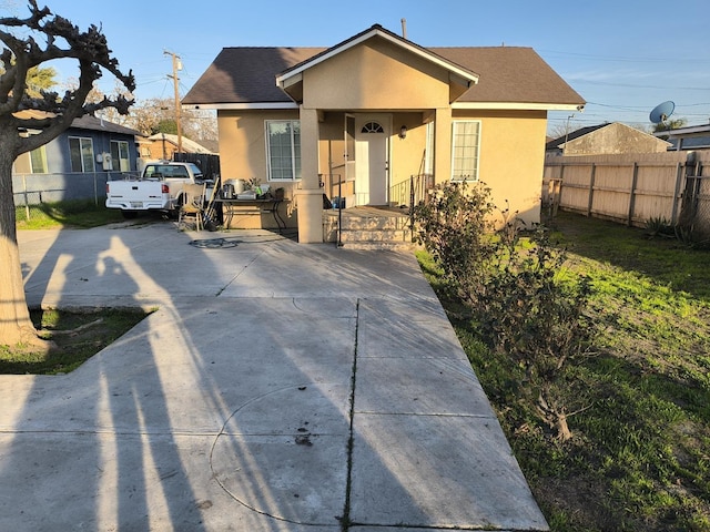 bungalow-style house with roof with shingles, fence, and stucco siding