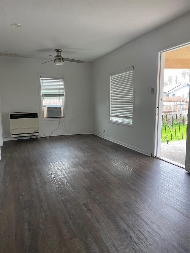 unfurnished living room featuring baseboards, visible vents, ceiling fan, dark wood-type flooring, and heating unit