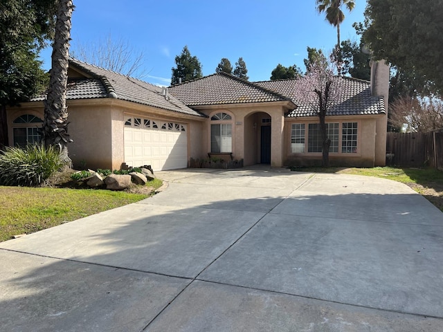 mediterranean / spanish house featuring a garage, fence, a tiled roof, concrete driveway, and stucco siding