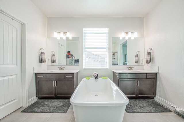 full bath with tile patterned flooring, a freestanding tub, two vanities, and a sink