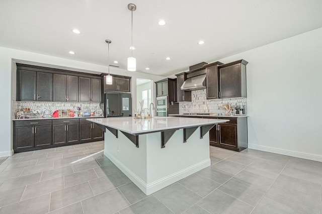 kitchen with a large island, wall chimney exhaust hood, light countertops, dark brown cabinetry, and a kitchen bar