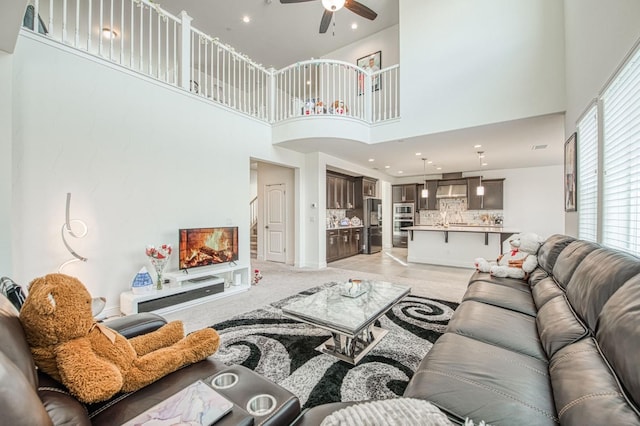 living area featuring ceiling fan, a high ceiling, a fireplace, and recessed lighting