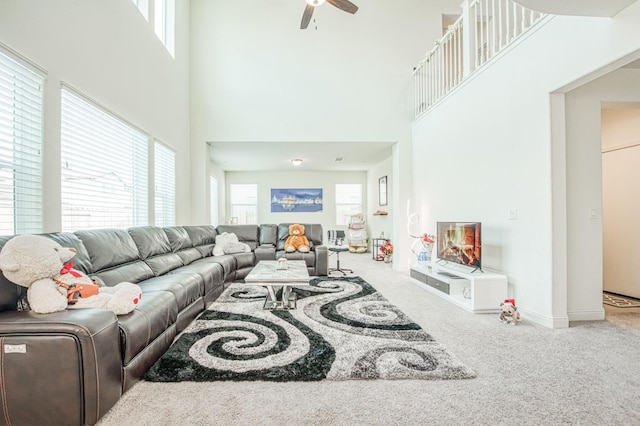 living room featuring baseboards, carpet, a ceiling fan, and a wealth of natural light