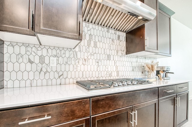 kitchen featuring stainless steel gas cooktop, custom exhaust hood, light countertops, decorative backsplash, and dark brown cabinetry