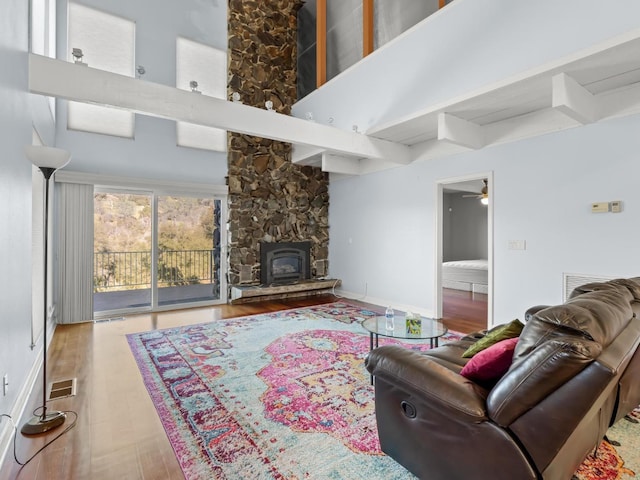 living room with visible vents, a towering ceiling, wood finished floors, beamed ceiling, and baseboards