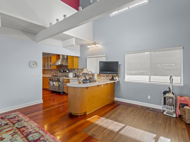 kitchen with dark wood-type flooring, high end stainless steel range, a peninsula, wall chimney range hood, and backsplash