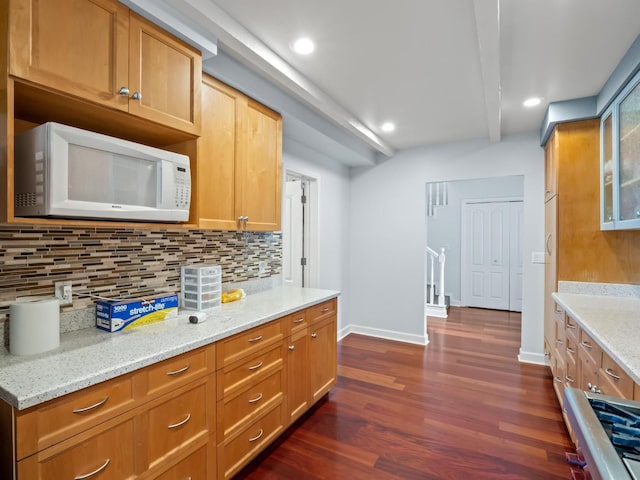 kitchen featuring white microwave, light stone countertops, dark wood-style floors, tasteful backsplash, and glass insert cabinets