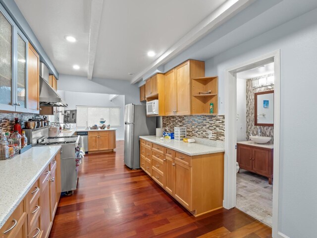 kitchen featuring dark wood finished floors, glass insert cabinets, light stone countertops, stainless steel appliances, and wall chimney range hood