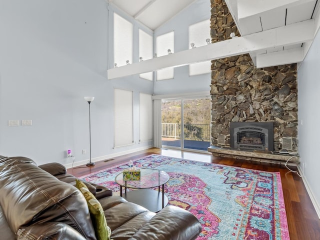 living room featuring visible vents, a towering ceiling, a stone fireplace, wood finished floors, and baseboards