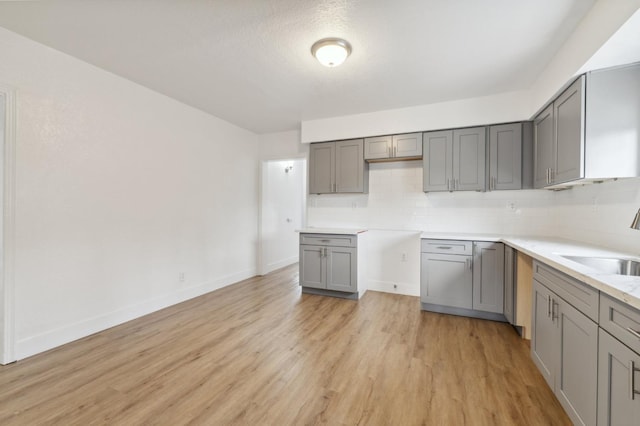 kitchen with light wood-type flooring, tasteful backsplash, gray cabinets, and a sink