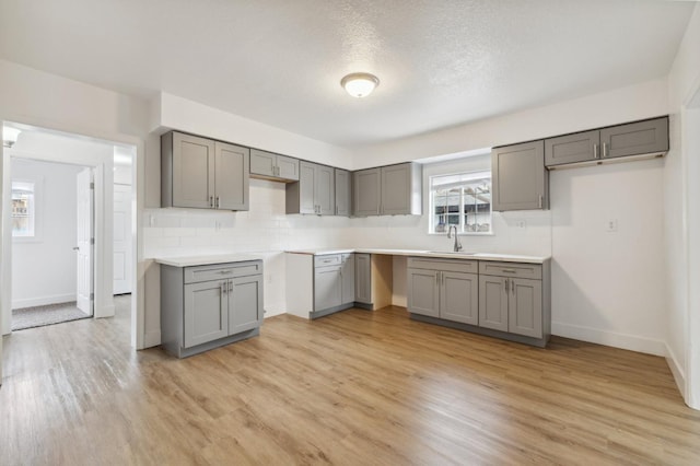 kitchen featuring light wood-type flooring, backsplash, a sink, and gray cabinetry