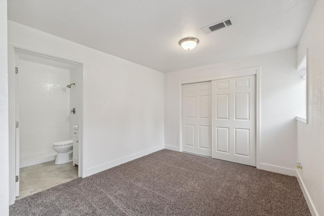 unfurnished bedroom featuring baseboards, visible vents, ensuite bath, carpet, and a closet