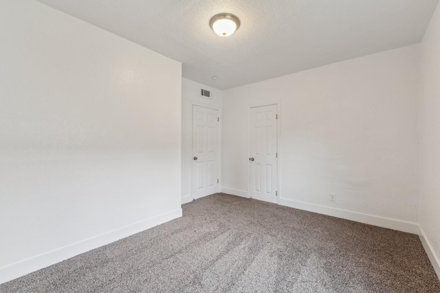 carpeted empty room with a textured ceiling, visible vents, and baseboards