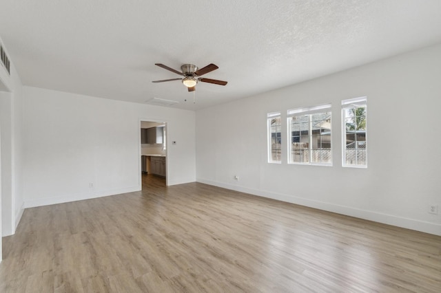 empty room featuring a ceiling fan, light wood-type flooring, a textured ceiling, and baseboards