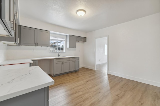 kitchen with light stone countertops, light wood-style flooring, gray cabinets, and a sink