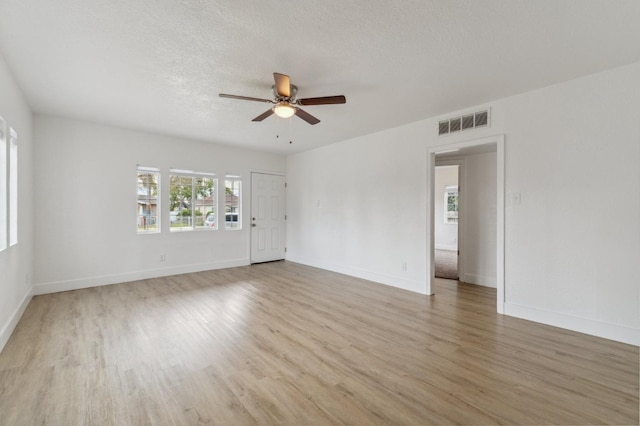 empty room with light wood-style floors, visible vents, a textured ceiling, and baseboards