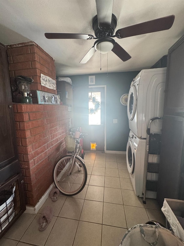 laundry room with a textured ceiling, light tile patterned flooring, laundry area, brick wall, and stacked washer and clothes dryer