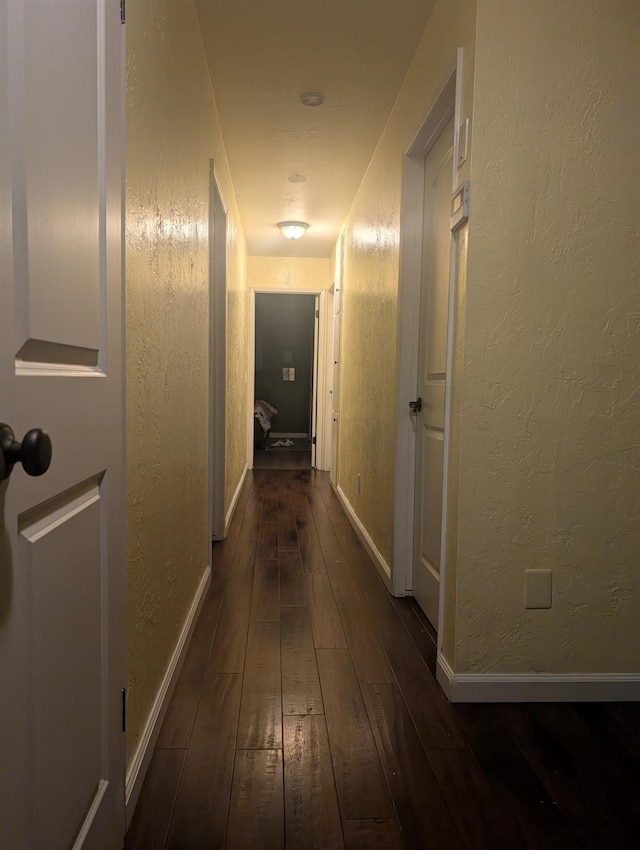 hall with dark wood-style floors, a textured wall, and baseboards