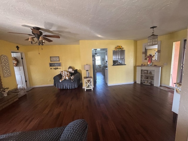 unfurnished living room with ceiling fan, a textured ceiling, wood finished floors, and baseboards